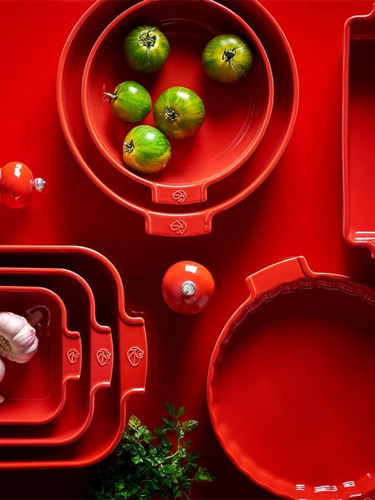 Eclectic Appolia red ceramic soufflé dishes and baking pans arranged on a matching red surface with fresh produce.