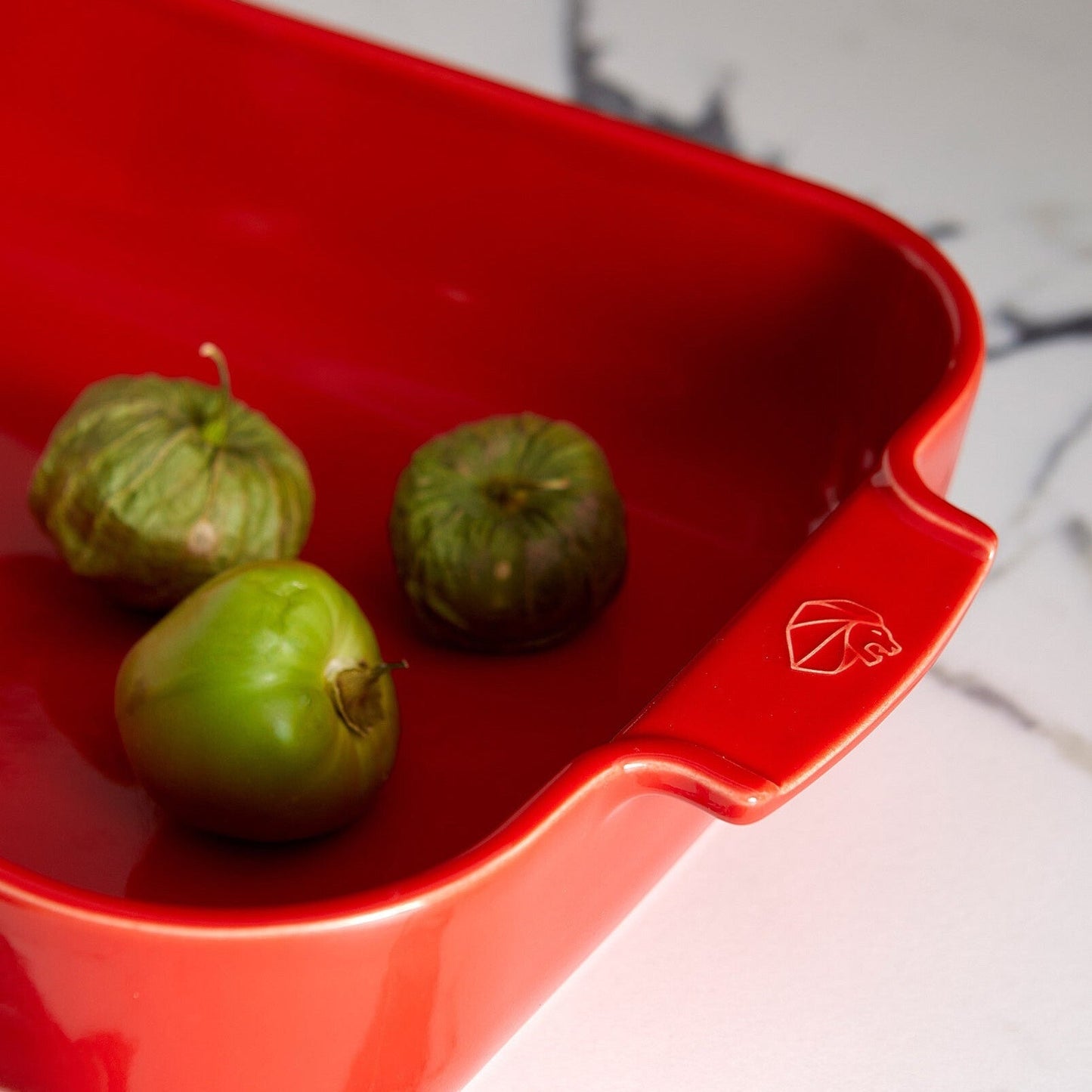 Eclectic Appolia rectangular ceramic oven dish in rich red with ribbed handles and three green tomatillos inside.