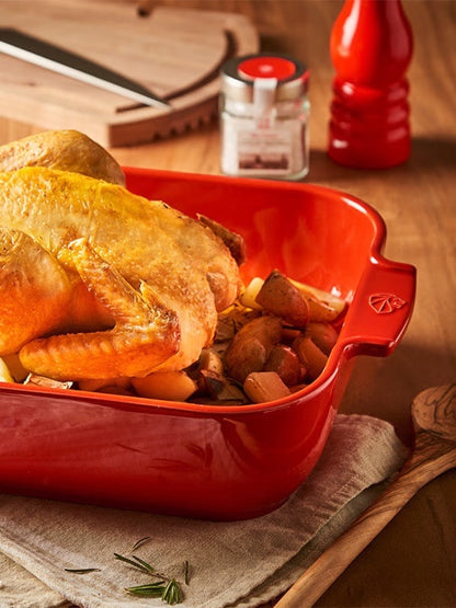 Eclectic Appolia rectangular ceramic oven dish in rich red holding a roasted chicken with potatoes on a kitchen table