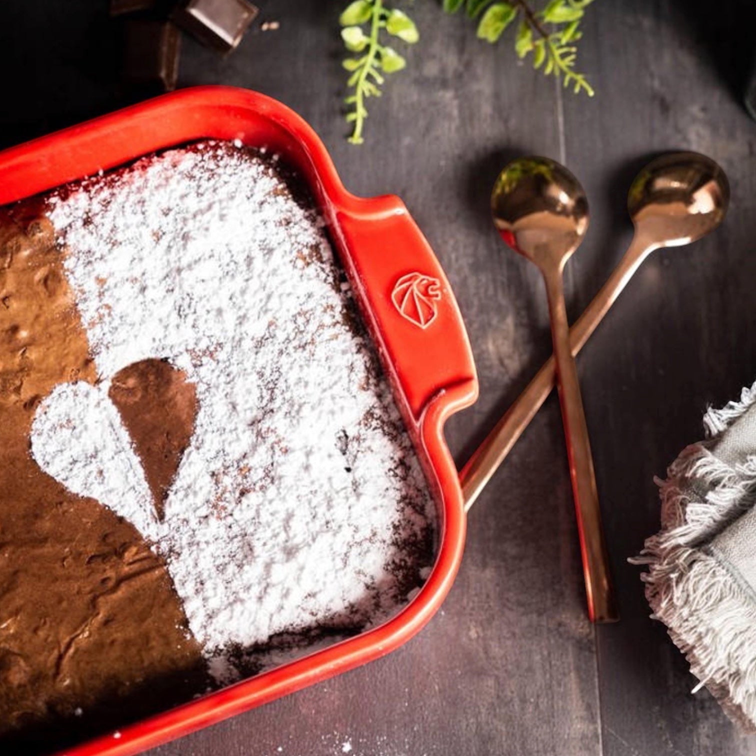 Eclectic Appolia red ceramic square oven dish filled with chocolate cake, featuring ribbed handles and a heart design.