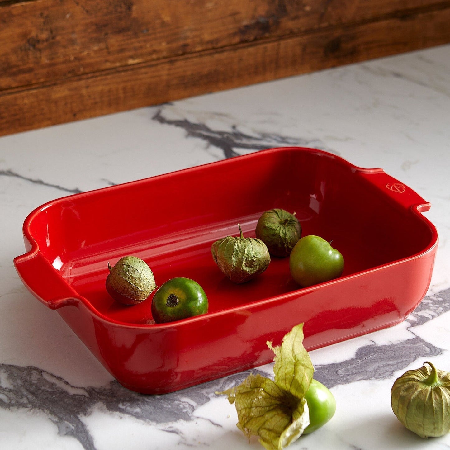 Eclectic Appolia rectangular ceramic oven dish in rich red with ribbed handles on a marble countertop with tomatillos