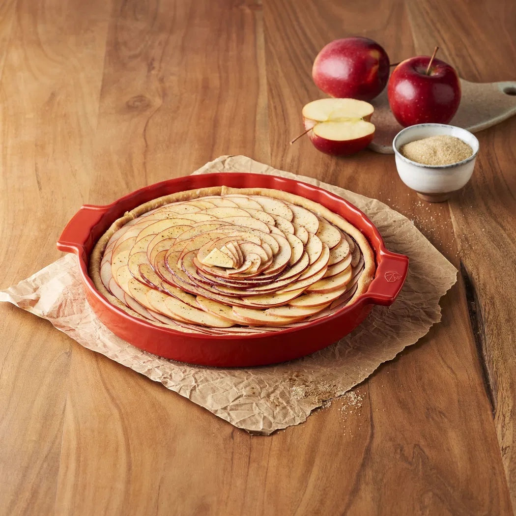 Eclectic Appolia 33 cm red ceramic pie dish filled with a sliced apple tart on a rustic wooden table.