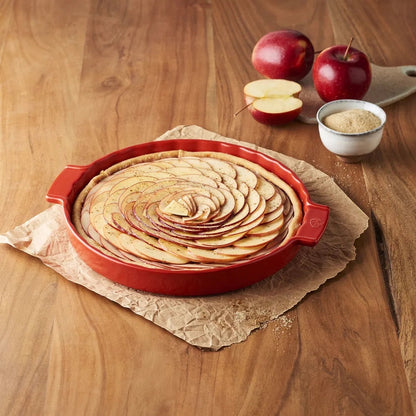 Eclectic Appolia 33 cm red ceramic pie dish filled with a sliced apple tart on a rustic wooden table.