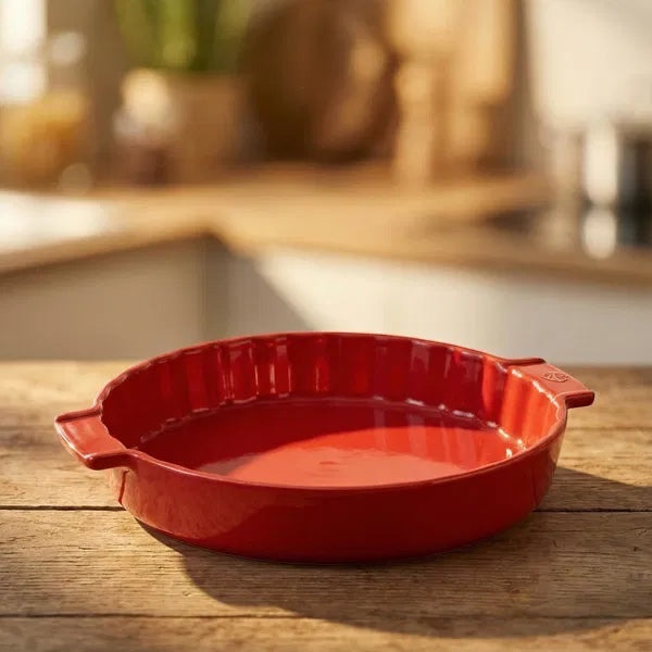 Eclectic Appolia 33 cm ceramic pie dish in rich red with a fluted edge, sitting on a rustic wooden kitchen table.