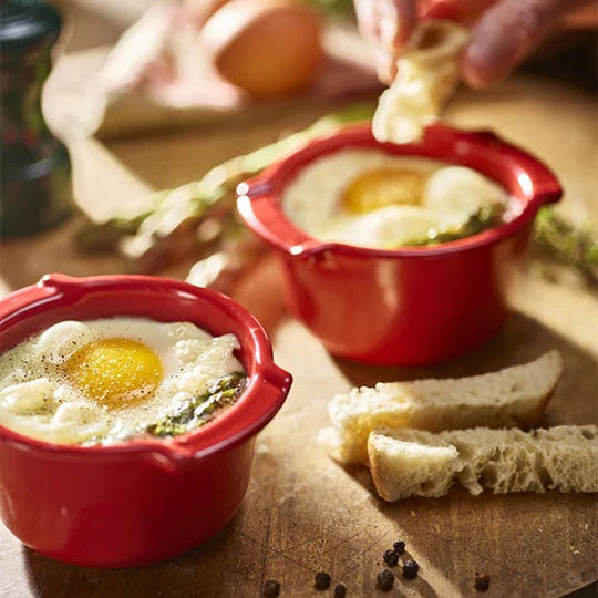 Eclectic Appolia rich red glazed ceramic ramekins filled with baked eggs and asparagus on a wooden board