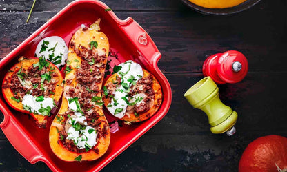 Eclectic Appolia red square ceramic oven dish filled with roasted stuffed squash on a dark wooden table.