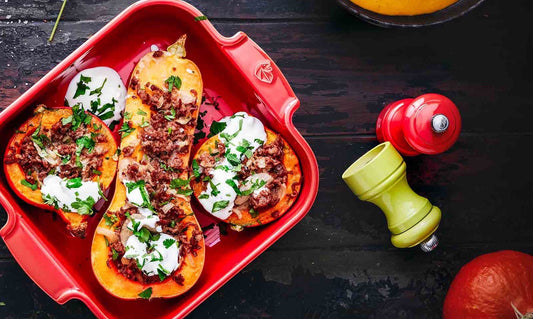 Eclectic Appolia red square ceramic oven dish filled with roasted stuffed squash on a dark wooden table.