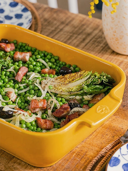 Eclectic Appolia rectangular ceramic oven dish in saffron yellow filled with a pea, bacon, and lettuce dish on a table