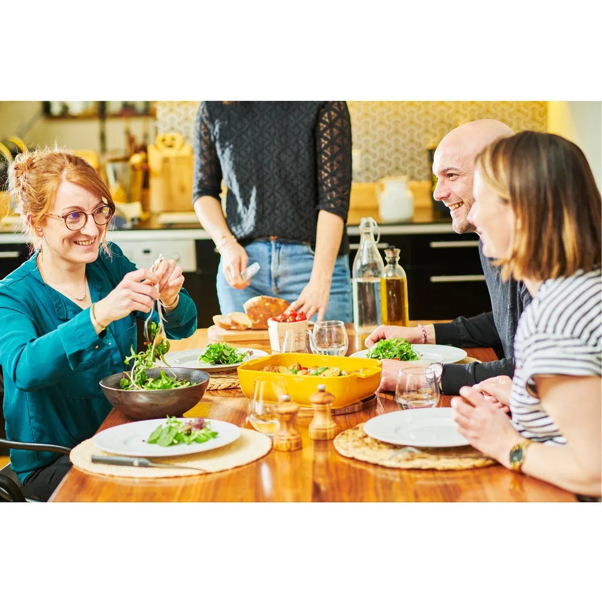 Friends enjoying a meal around a table with a bright saffron yellow Appolia rectangular ceramic oven dish