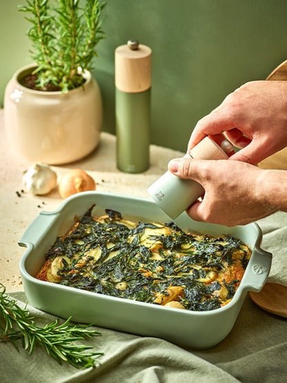 Eclectic Appolia rectangular ceramic oven dish in sage green filled with a baked vegetable gratin on a kitchen table.