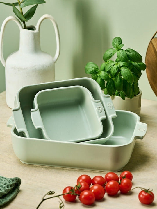 Eclectic Appolia square ceramic oven dishes in sage green, nested for storage with ribbed handles on a wooden table.
