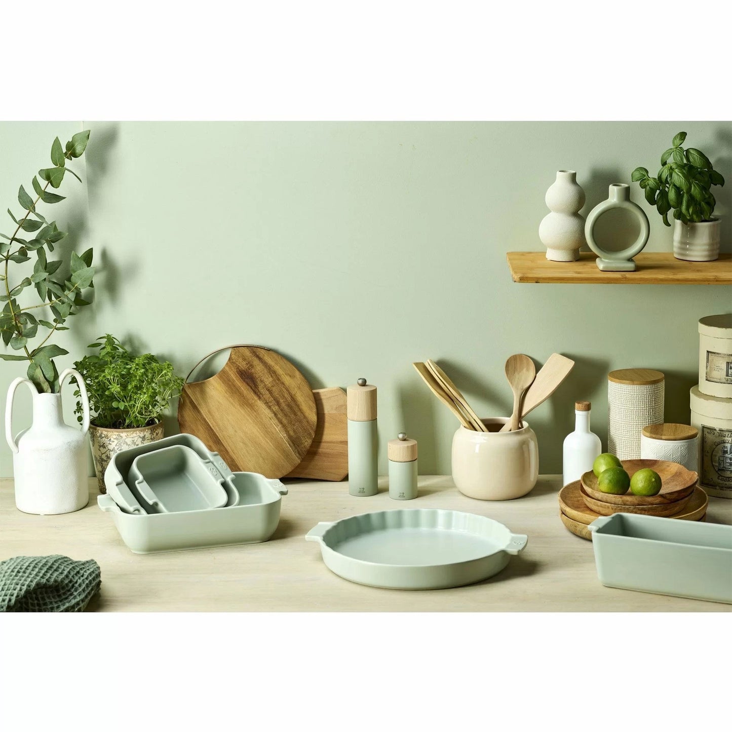 Eclectic collection of Appolia sage green ceramic oven dishes and kitchenware arranged on a wooden table.