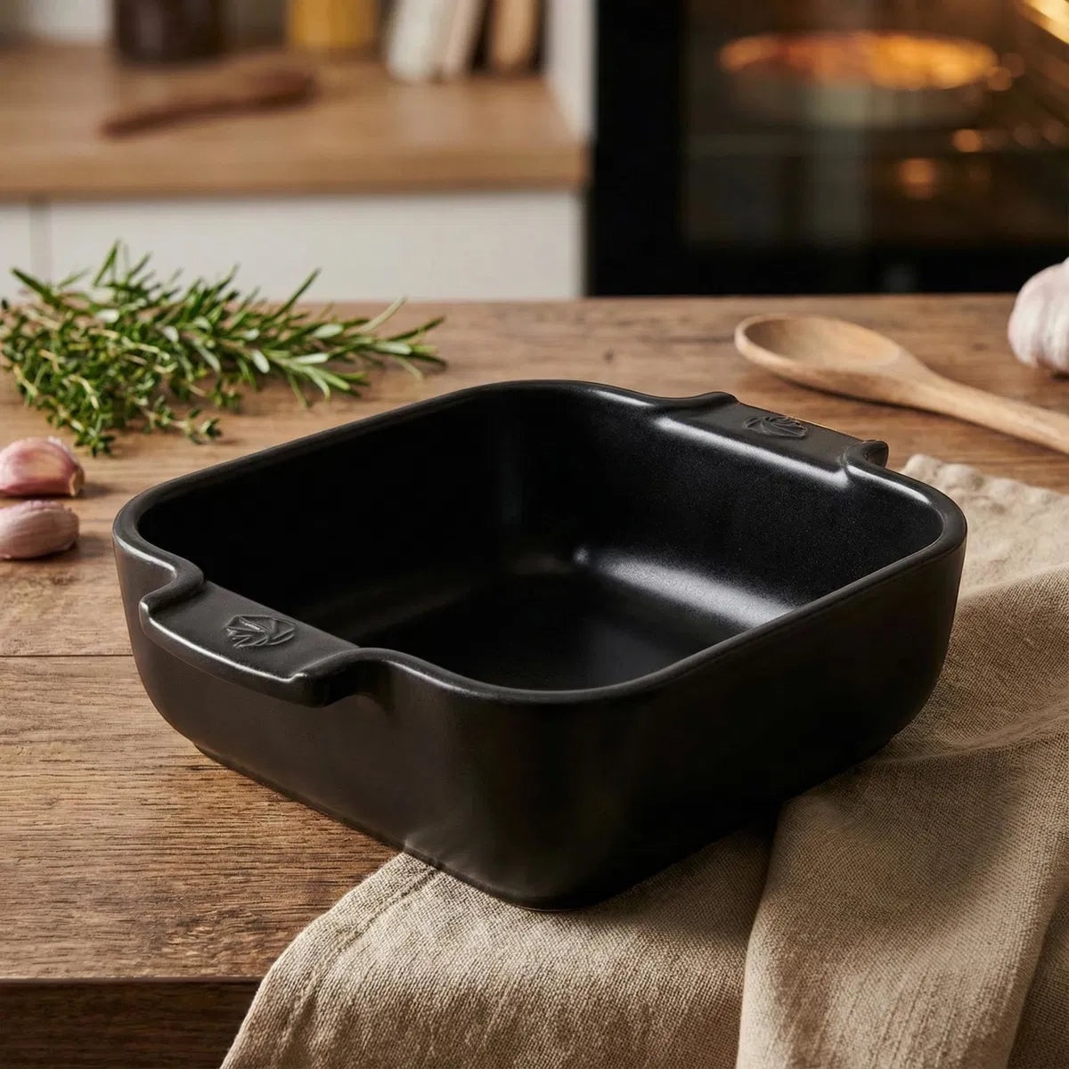 Eclectic Appolia square ceramic oven dish in satin black with ribbed handles on a wooden kitchen table.