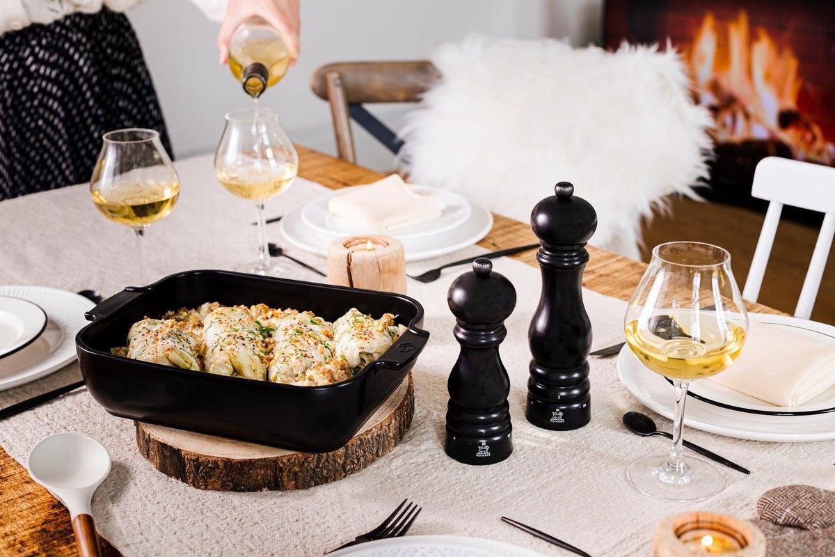 Eclectic Appolia satin black square ceramic oven dish filled with food on a rustic dining table with wine glasses.