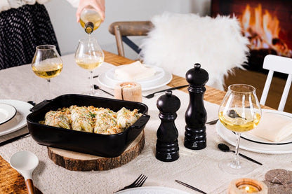 Eclectic Appolia satin black square ceramic oven dish filled with food on a rustic dining table with wine glasses.