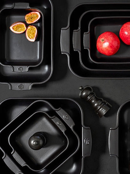 Eclectic Appolia rectangular ceramic oven dishes in satin black with ribbed handles, arranged with fruit and mills.