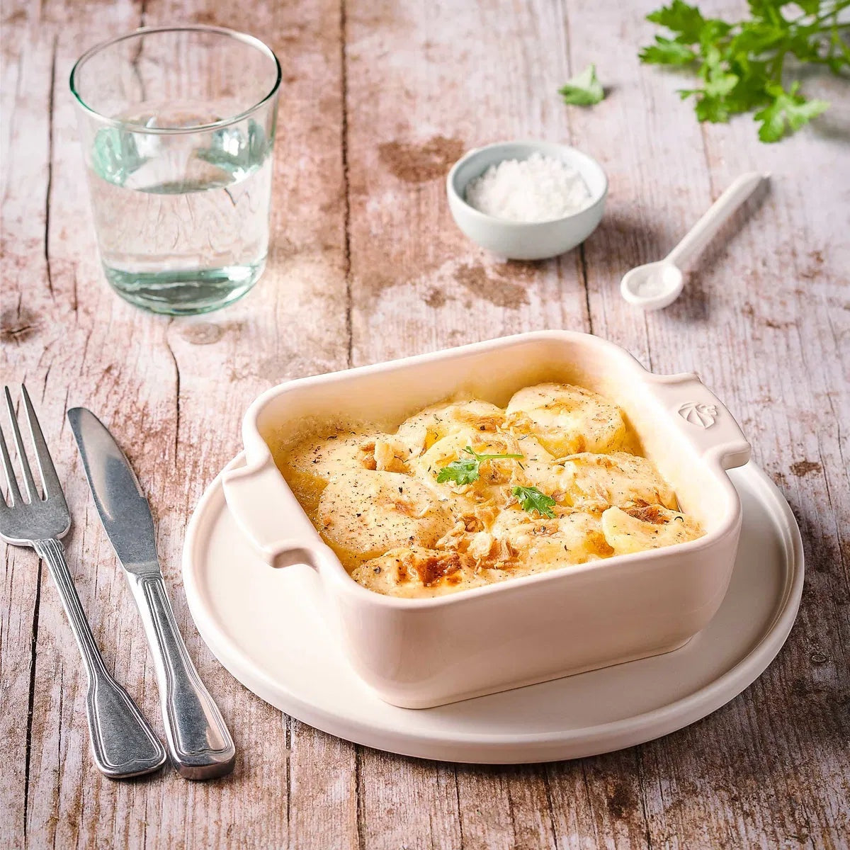 Eclectic Appolia square ceramic oven dish in ecru cream filled with a potato gratin on a rustic wooden table