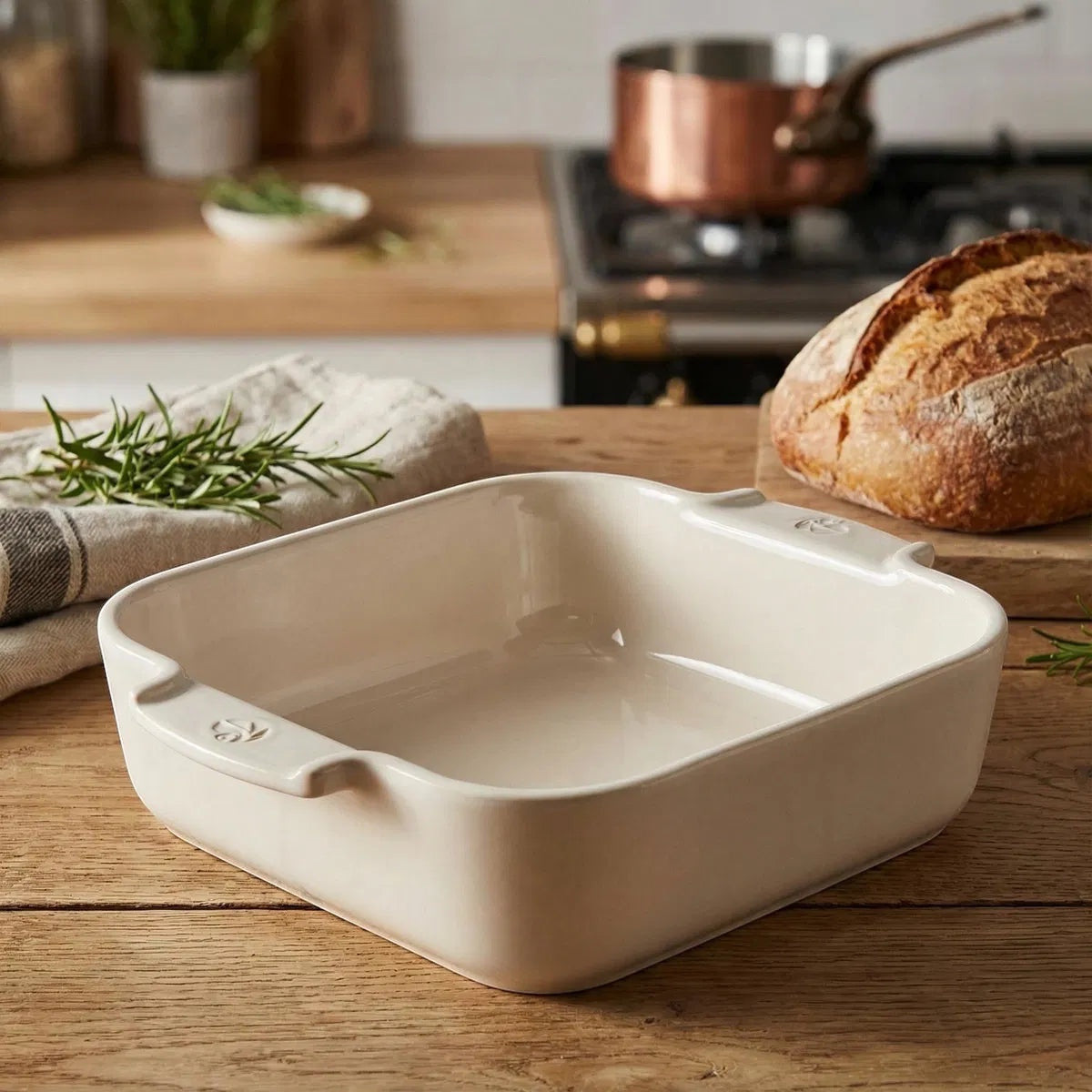 Eclectic Appolia square ceramic oven dish in ecru cream with ribbed handles on a rustic wooden kitchen table.