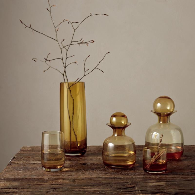 Eclectic ASA Selection Ajana amber mouth-blown glass vase and glassware set on a rustic wooden table.