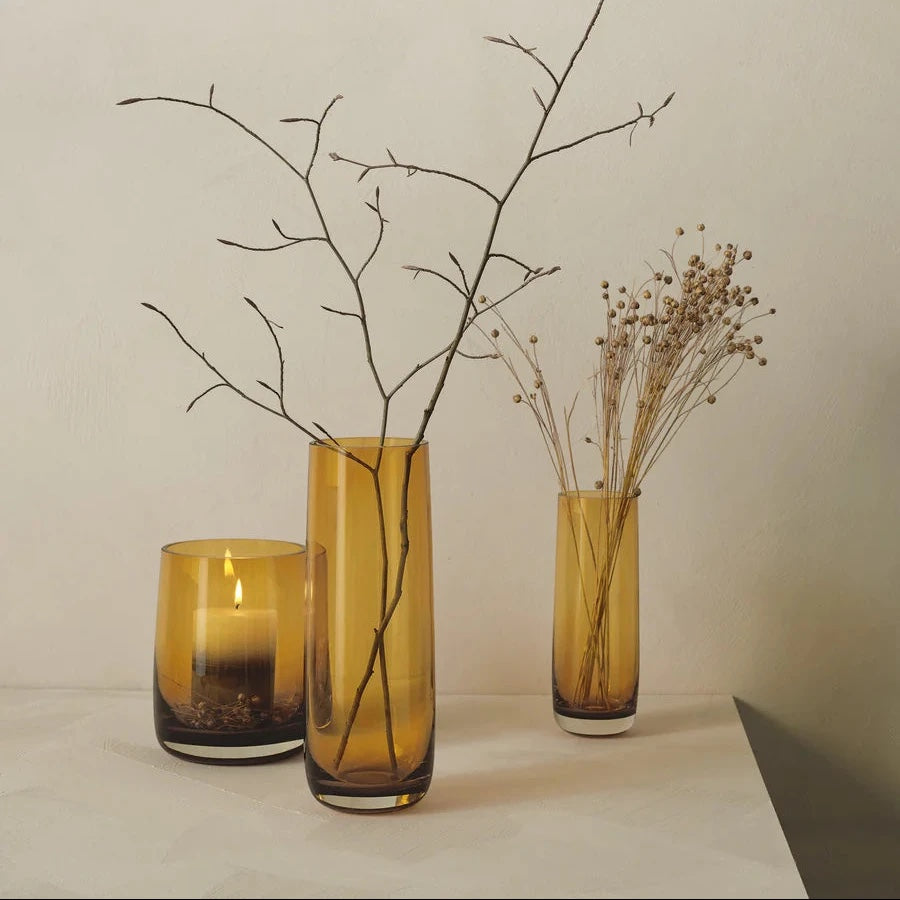 Eclectic ASA Selection Ajana amber glass vases and candle holder with dried branches on a white surface