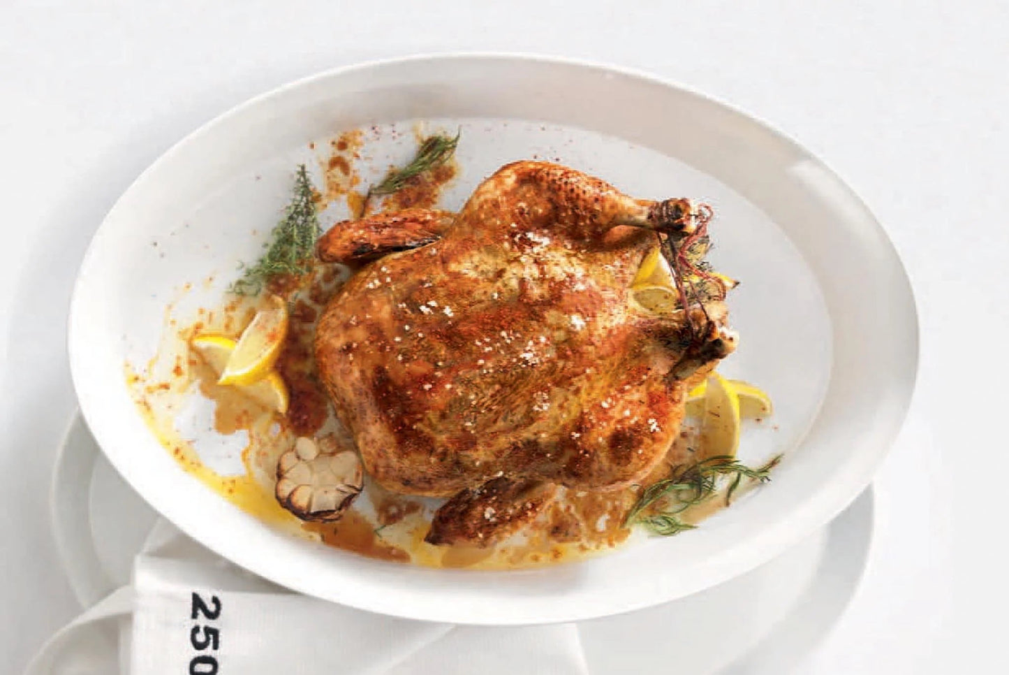 Eclectic ASA Selection white porcelain oval roasting dish containing a whole roasted chicken with herbs and lemon