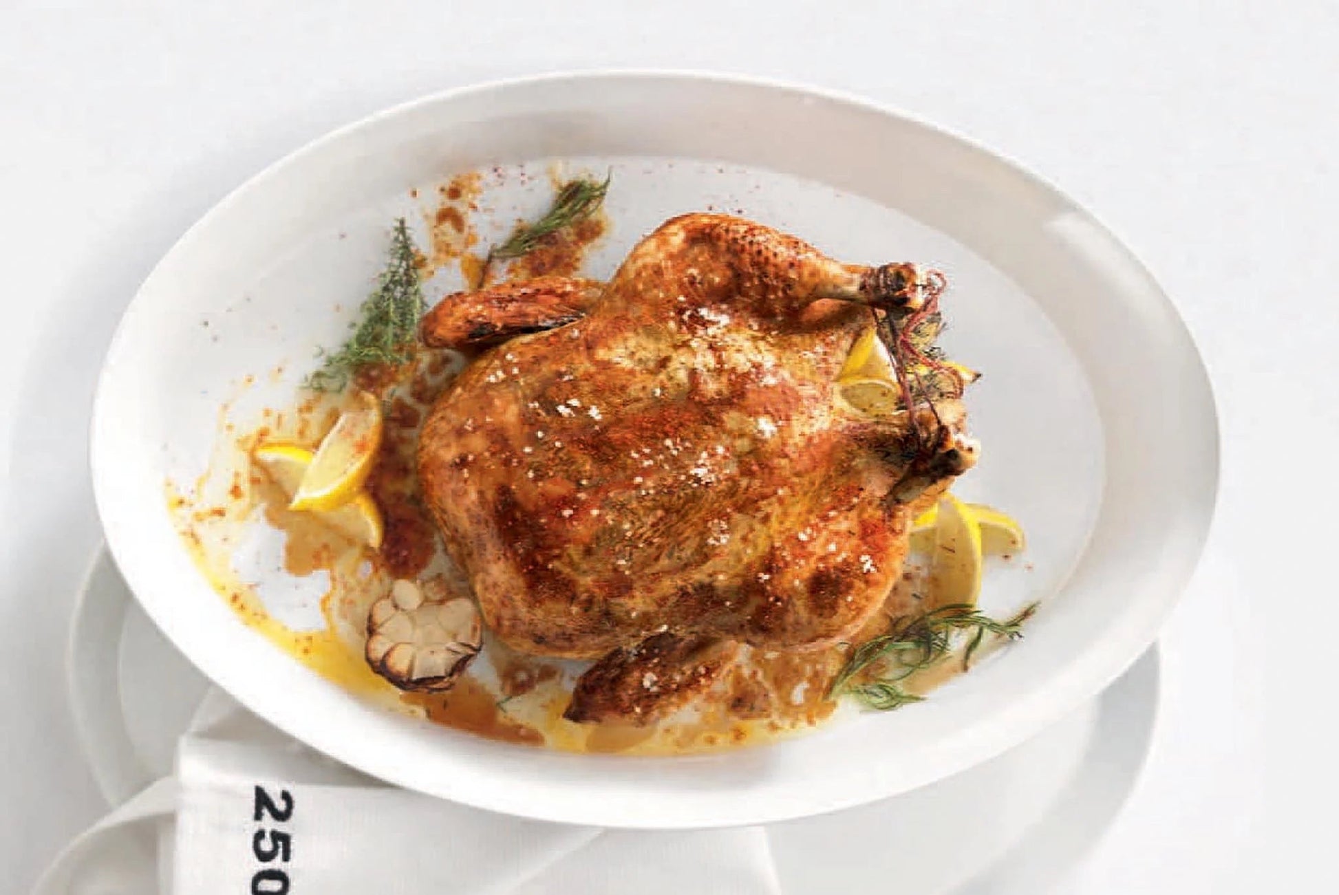Eclectic ASA Selection white porcelain oval roasting dish containing a whole roasted chicken with herbs and lemon