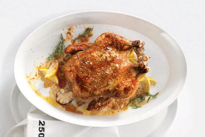Eclectic ASA Selection white porcelain oval roasting dish containing a whole roasted chicken with herbs and lemon