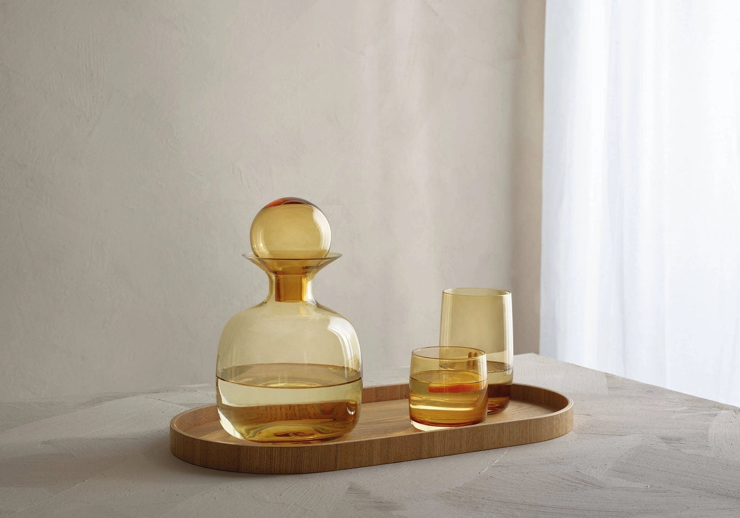 Eclectic ASA Selection Sarabi amber mouth-blown glass carafe with spherical stopper on a wooden tray with matching glasses