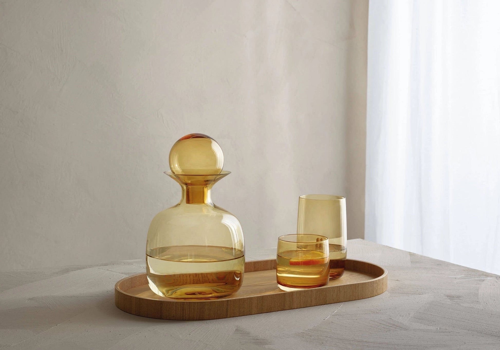 Eclectic ASA Selection Sarabi amber mouth-blown glass carafe with spherical stopper on a wooden tray with matching glasses