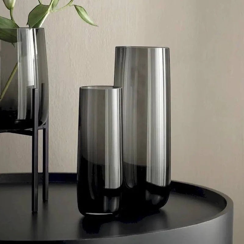 Eclectic ASA Selection Ajana smoky grey mouth-blown glass vases with cylindrical silhouettes on a black table.