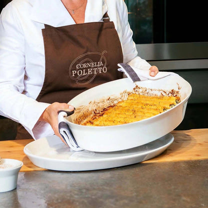Eclectic ASA Selection white porcelain oval roasting dish held by a chef in a kitchen for oven-to-table serving.