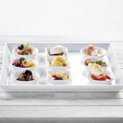 Eclectic ASA Selection white porcelain square serving platter displaying assorted small desserts on a wooden table.