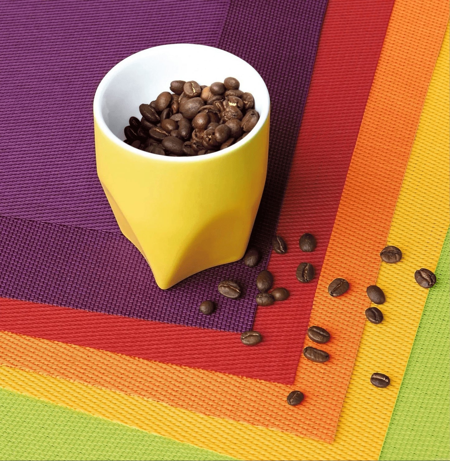 Eclectic ASA Selection plum, red, orange, and lime green PVC placemats stacked with a yellow cup of coffee beans
