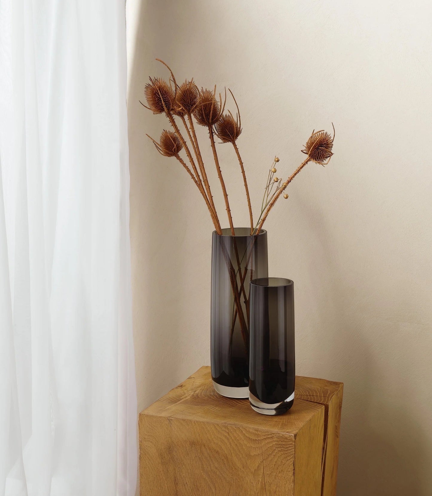 Eclectic ASA Selection Ajana smoky grey mouth-blown glass vases in two sizes styled with dried stems on a wooden block