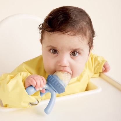 Eclectic B.Box blue silicone fresh food feeder held by a baby in a yellow bib for safe self-feeding