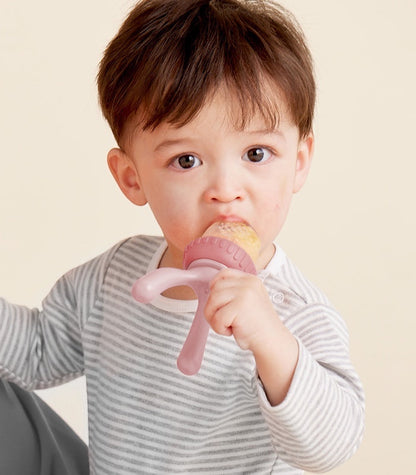 Eclectic B.Box blush silicone fresh food feeder held by a toddler in a striped shirt for safe self-feeding