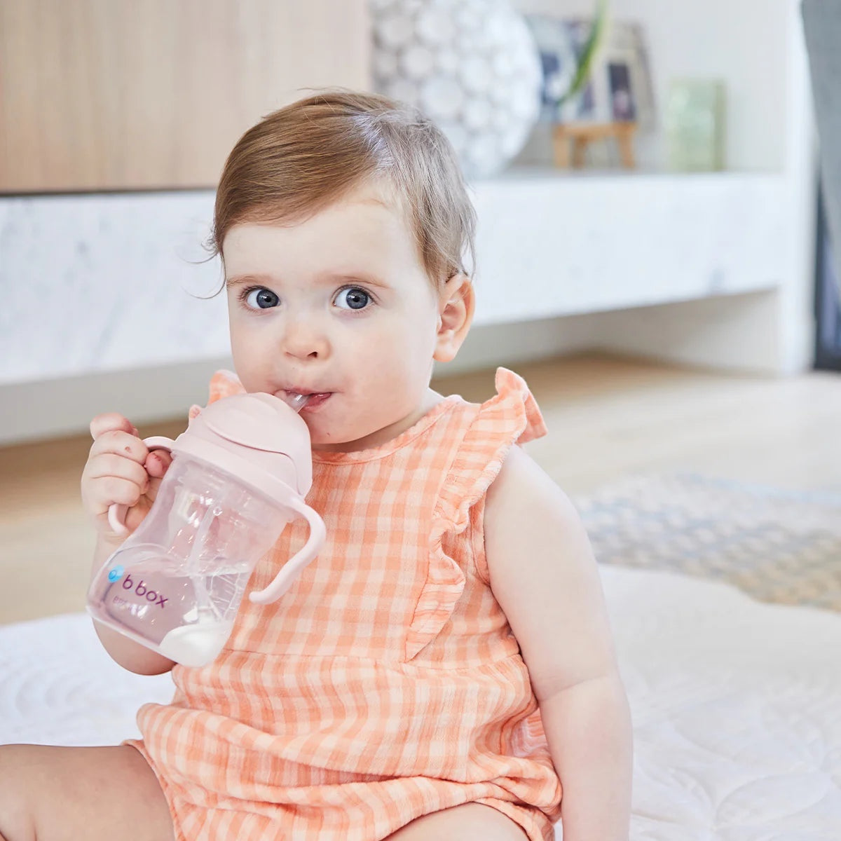 Toddler drinking from a blush Eclectic b.box weighted straw sippy cup with easy-grip handles in a bright home setting