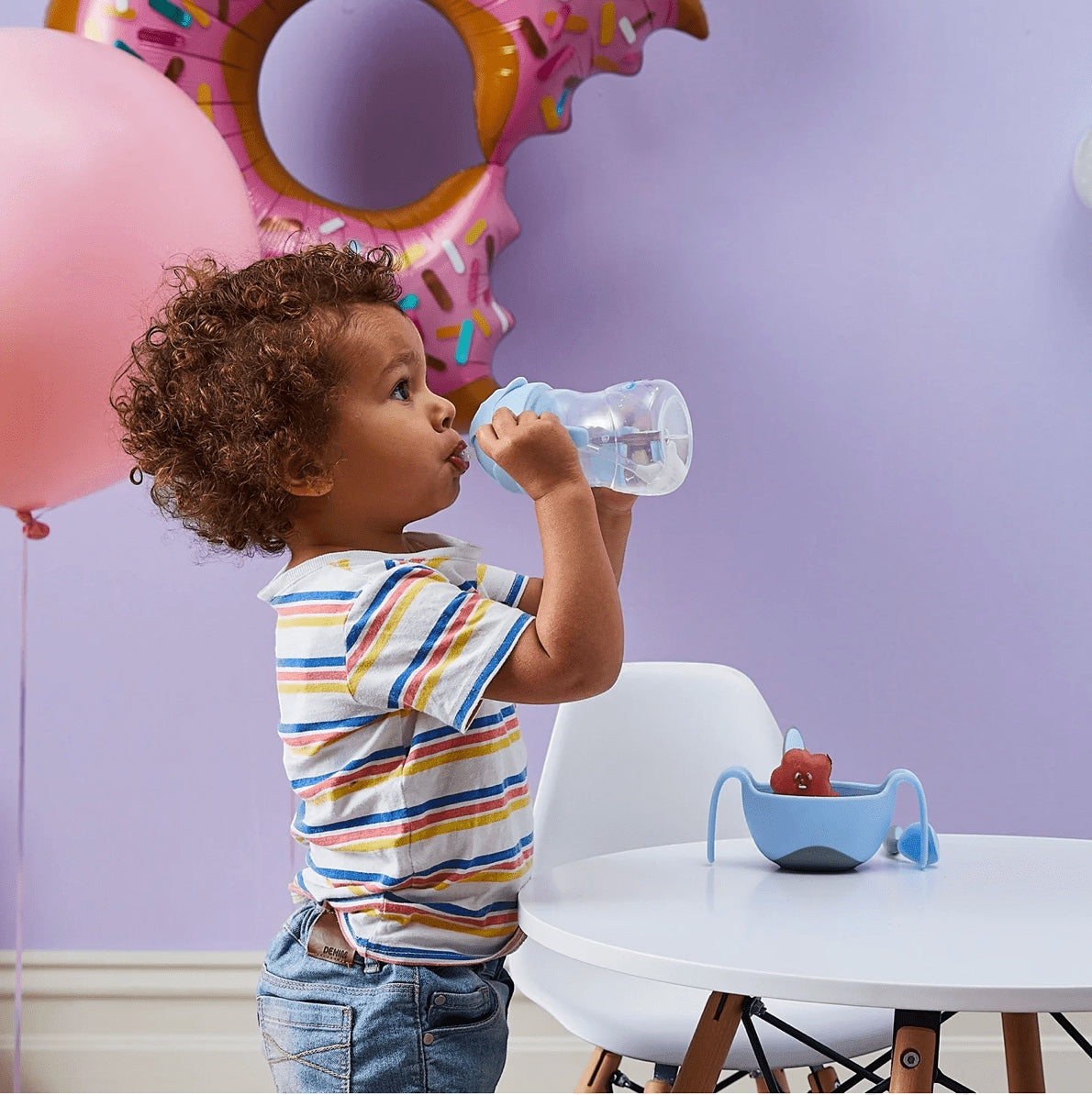 Eclectic b.box bubblegum sippy cup with weighted straw held by a toddler in a playful party-themed room.