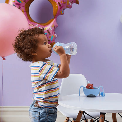 Eclectic b.box bubblegum sippy cup with weighted straw held by a toddler in a playful party-themed room.