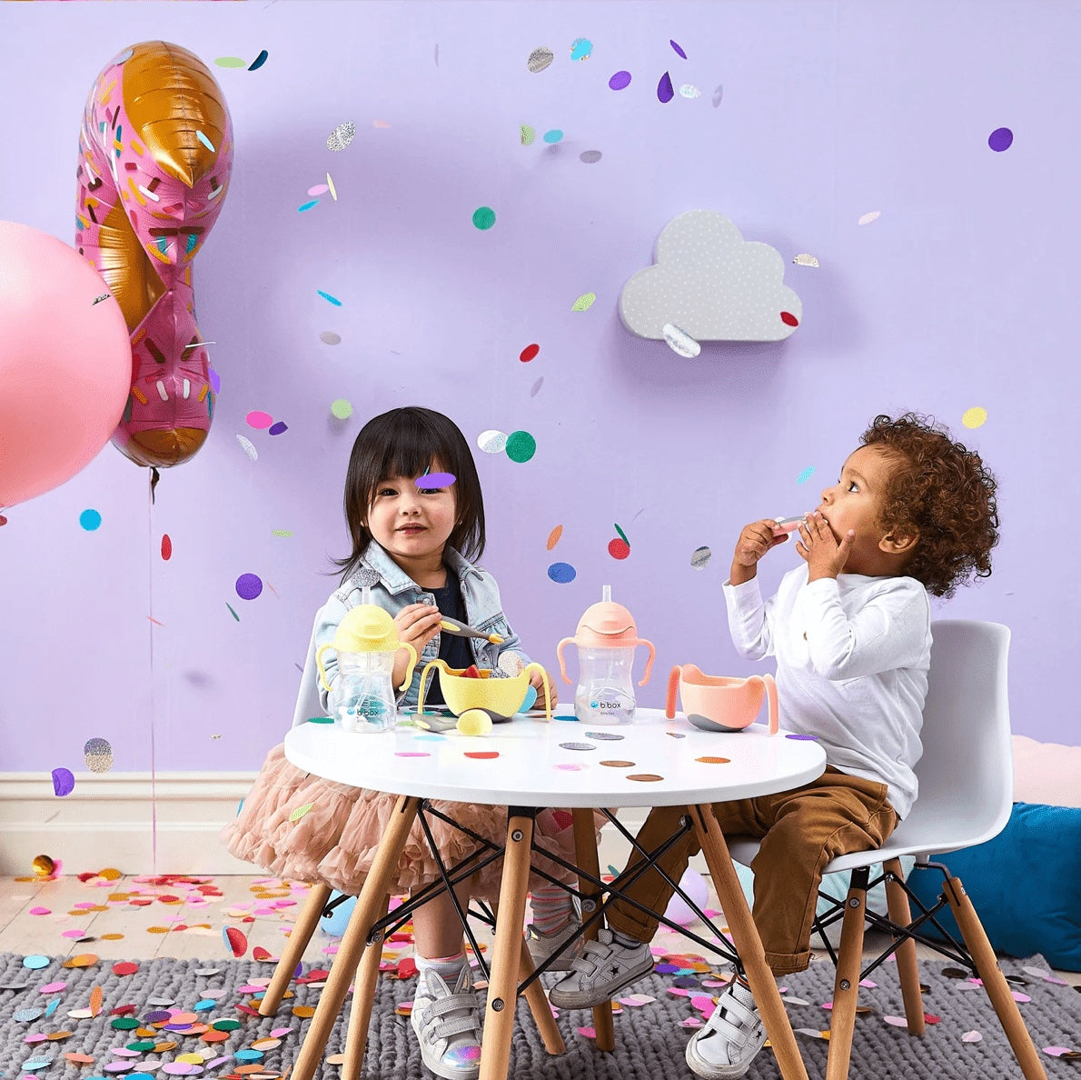 Eclectic b.box Tutti Frutti sippy cups on a table with two children at a party with balloons and confetti