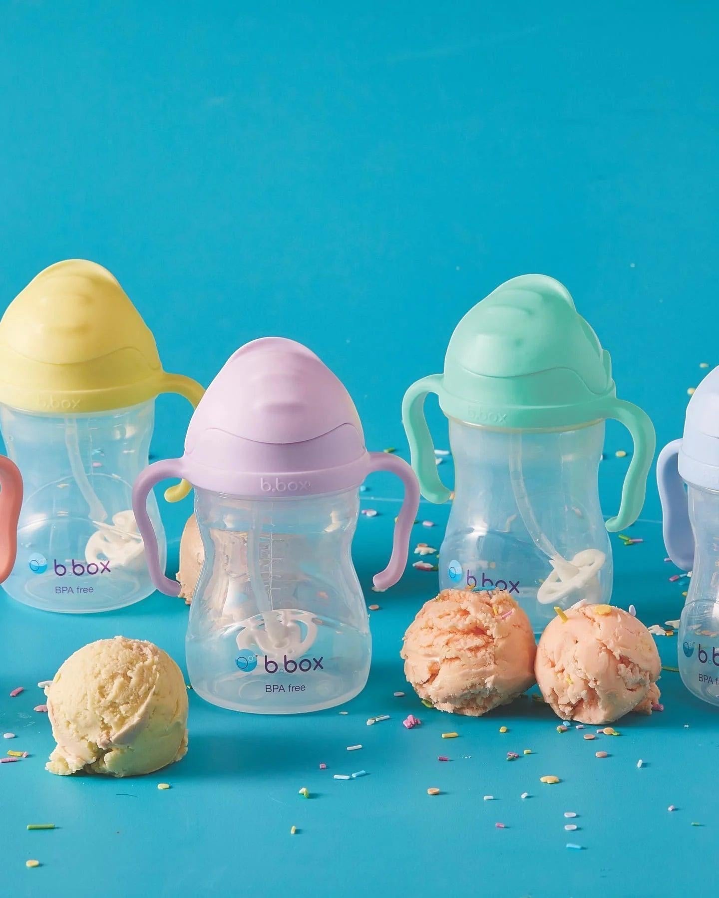Eclectic b.box weighted straw sippy cups in pastel colours with easy-grip handles on a blue background with ice cream