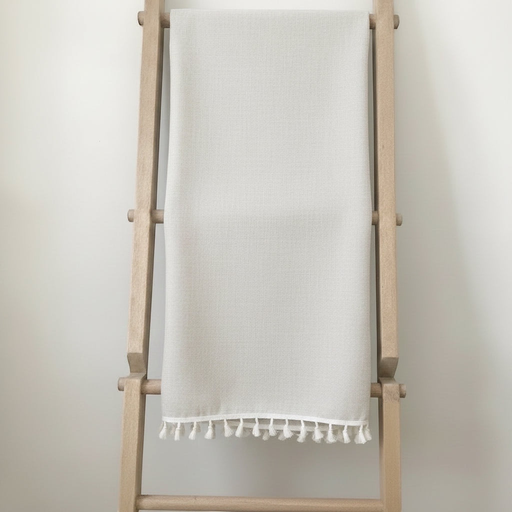 Eclectic light beige linen blend tablecloth with decorative tassel edging draped over a wooden ladder