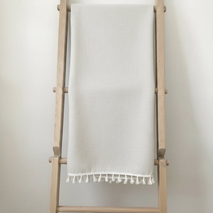 Eclectic light beige linen blend tablecloth with decorative tassel edging draped over a wooden ladder