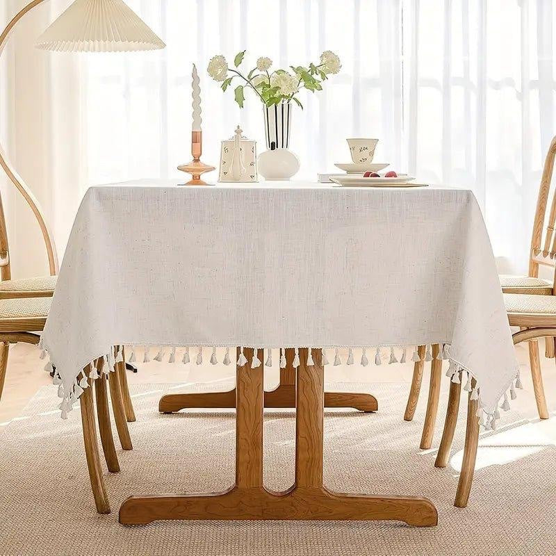 Eclectic light beige linen blend rectangular tablecloth with decorative tassel trim on a wooden dining table