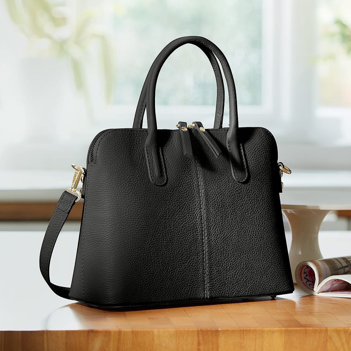 Eclectic Bella structured black Italian leather handbag with silver hardware and top handles on a wooden table.