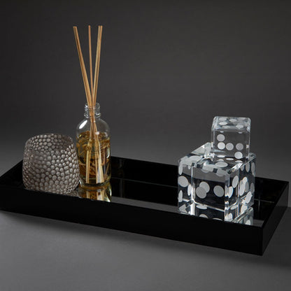 Eclectic black acrylic mirrored display tray holding a reed diffuser and decorative dice on a dark background.