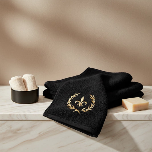 Eclectic black cotton guest towel with gold embroidered crown detail folded on a marble surface with soap