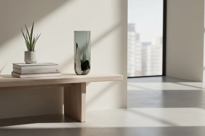 Eclectic black and white glass cylinder vase on a wooden bench in a bright, minimalist room.