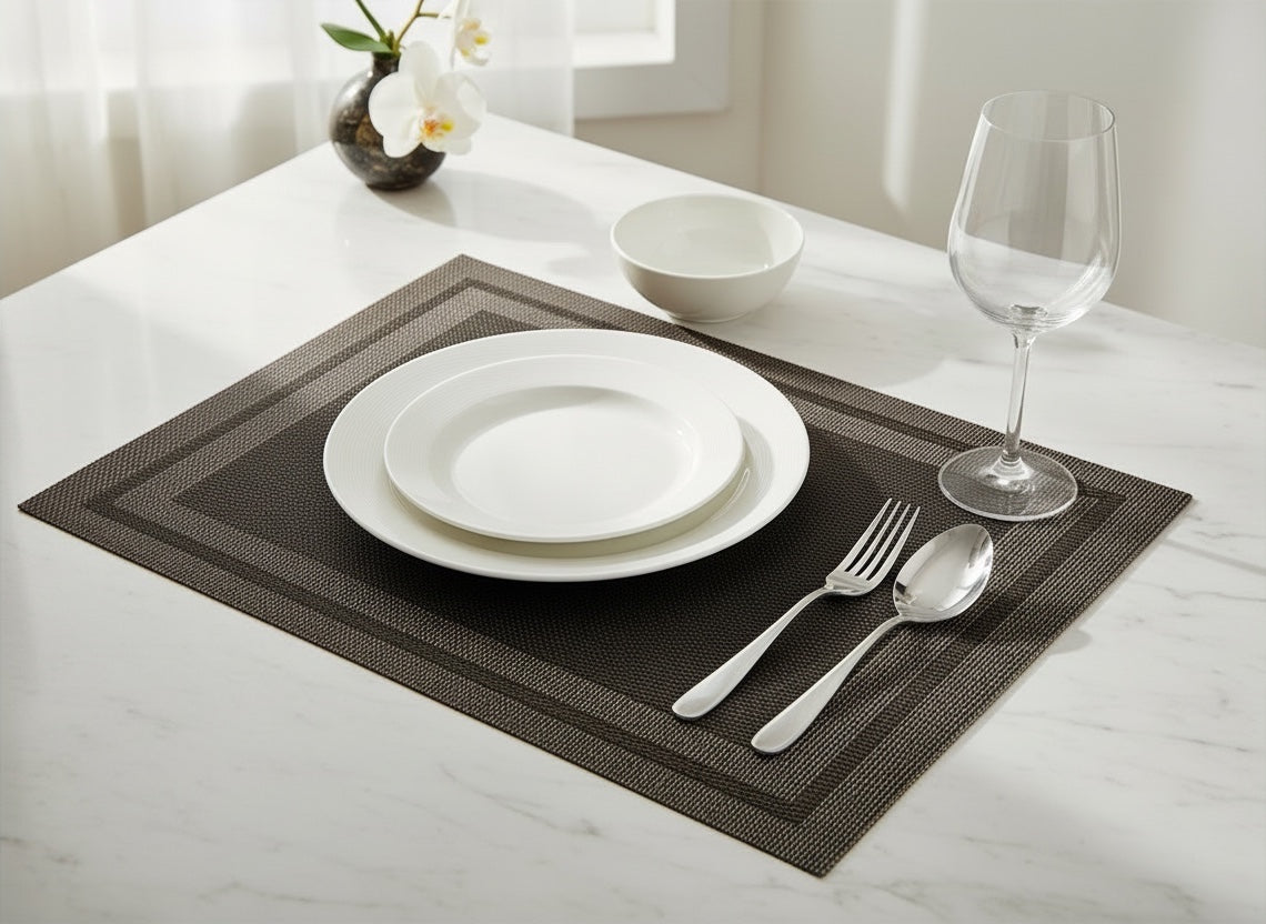 Eclectic black woven PVC rectangular placemat set with white ceramic plates and silverware on a marble table.