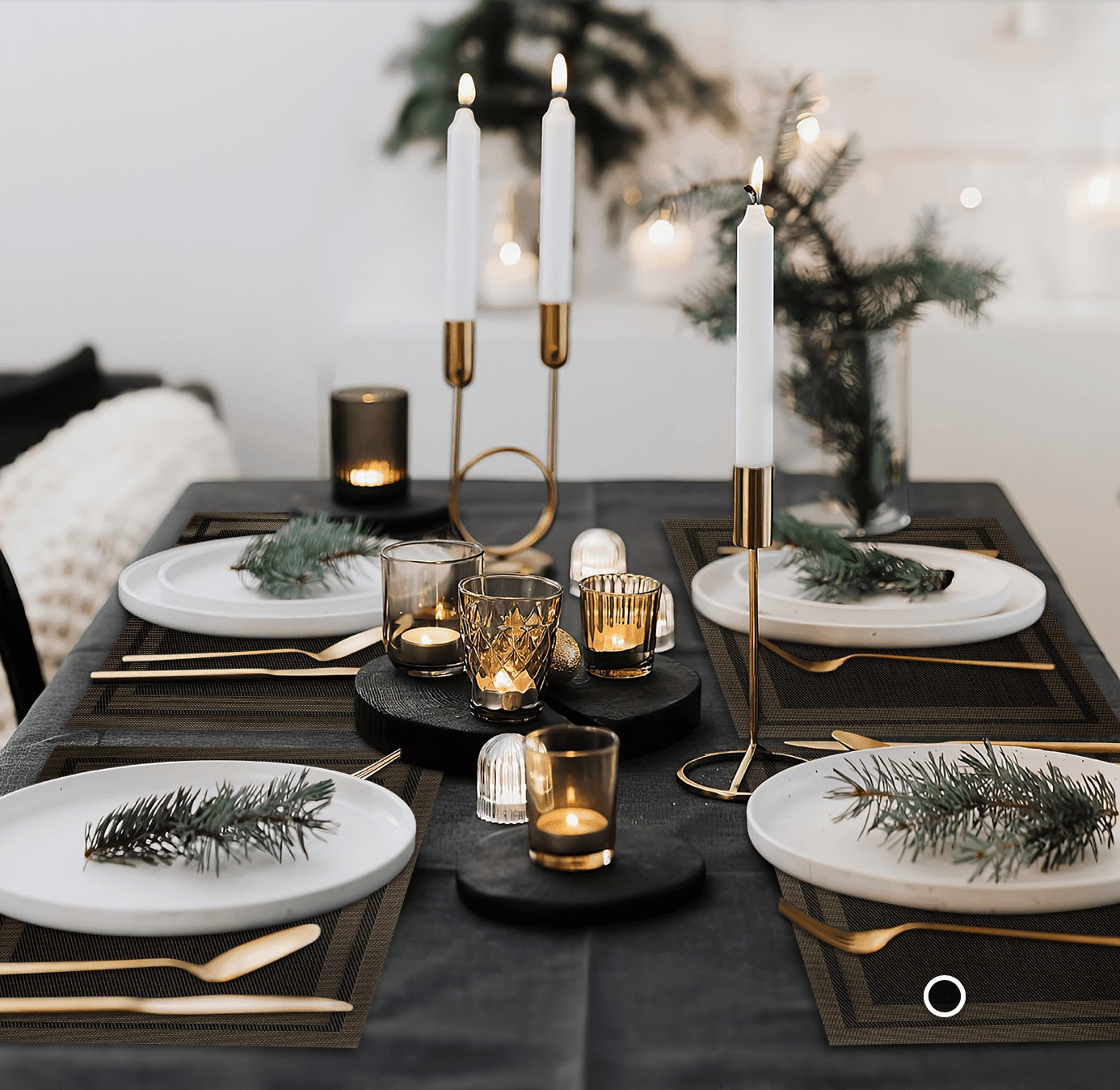 Eclectic black woven PVC placemats set on a dining table with white plates, gold cutlery, and festive holiday decor.